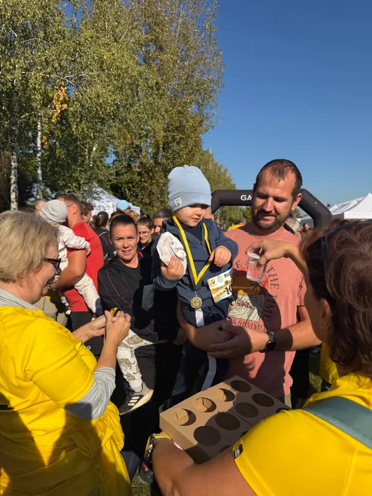 Kisgyerek kapja meg az érmét a sárga mellényes segítőktől