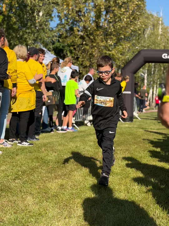 Rajtszámos kisfiú a gyerekfutamon, háttérben a sárga mellényes segítők